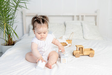 baby girl playing with wooden toy cubes on the bed at home in a bright room, the concept of early childhood development