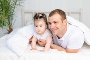 father and baby daughter on the bed under the blanket, smiling and hugging. Happy family, Father's Day