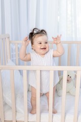 happy laughing baby girl in the crib in the nursery in a white bodysuit