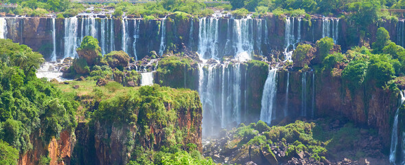 Iguazu waterfalls in Argentina, view from Devil's Mouth. Panoramic view of many majestic powerful water cascades with mist and splashes. Panoramic image of Iguazu valley with lush subtropical forest.