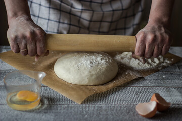italy men's hands roll out pizza dough with wooden rolling pin on wooden table