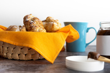Basket full of puff pastries with a cup of coffee and a jar of chocolate.Small spoon full of chocolate spread. Selective focus