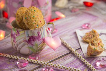 coconut cookies with colorful sprinkles in a cup on a pink wooden background with hearts around Valentine's day