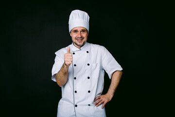 Chef cook wearing kitchen jacket and hat raising finger in ok sign on black background on black background