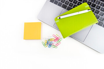 White office desk with open notebook, pen, colorful stickers, laptop and other office supplies.