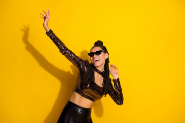 Photo of crazy young lady dance have fun raise hand wear sunglass glossy top isolated yellow color...