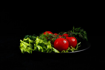 Fresh vegetables on a black plate, just from the garden, greens and tomatoes.