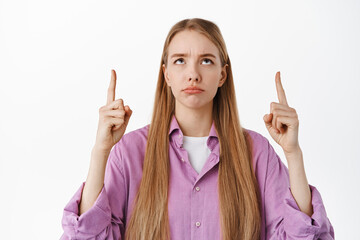 Skeptical girl looks disappointed and pointing up, sulking at unfair thing, feel regret or jealous...