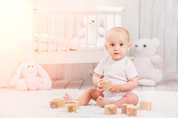 Little kid plays alone in his room with wooden cubes, against the background of an interior room 