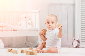 Little kid plays alone in his room with wooden cubes, against the background of an interior room 