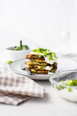 Potato pancakes with spinach, garlic and green onions served with sour cream dip on a plate on a light background 