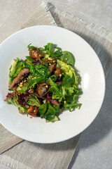 Summer salad with meat and lettuce, arugula and spinach, cherry tomatoes and cucumber on a white plate on a light background. Summer menu concept.