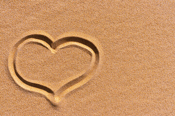 Fototapeta na wymiar The symbol of the heart drawn on a sand. Next to the drawing of the heart is copy space. Background close up of a golden sunny sandy beach. 