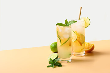 Two summer cold mojito cocktails with orange and lime slices on color white and beige background....