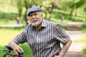 A positive, elderly man went for a walk to the park, stopped and an electric scooter was standing next to him. Summer, sunny day. Healthy lifestyle of the elderly.