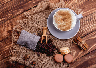 Fototapeta na wymiar grey cup of coffee, beans, cinnamon, macaroons and anise on the wooden background
