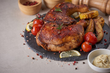 Grilled chicken legs in barbecue sauce and roasted vegetables with tomatoes, potatoes, pepper seeds, salt in black stone plate on black stone table. Top view, copy space. Tasty snack . Flat lay..
