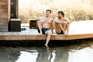 Company of male friends sitting on the terrace near the lake in the spa complex. Relax and fun time in wellness spa. 