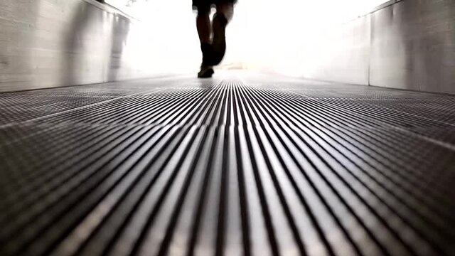 Steps of a man walking on an escalator, with unfocused and blurred background, at ground leve