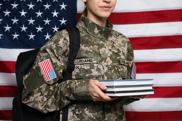 Female cadet with backpack and books against American flag, closeup. Military education