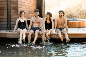 Company of friends sitting on the terrace and wetting their feet in the lake in the spa complex....