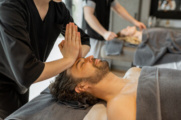 Obraz na płótnie Canvas Female masseur doing facial massage to a male client at Spa salon. Wellness and leisure concept.