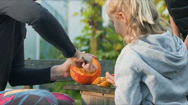 Handheld shot of a caucasian family, mother hollowing out and scraping down the inside pumpkin, son and daughter watching her