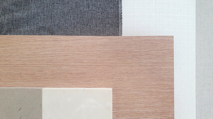 close up interior material board containing dark grey textile fabric ,white and gray woolen fabric laminated ,grey and beige grained artificial stone samples placed on oak wood veneer.