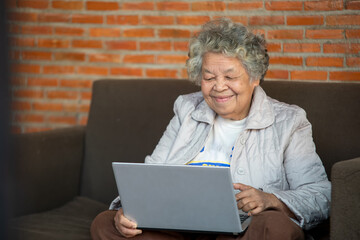 Happy senior woman sitting using computer laptop for spending leisure time on the couch at home.