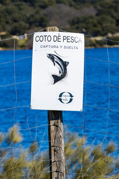CARTEL SOBRE POSTE DE MADERA CON INDICADOR DE COTO DE PESCA Y LAGO AZUL AL FONDO 