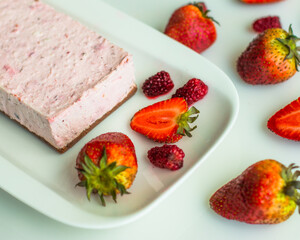 Pink cheese and red fruit cake with biscuit background, on a white plate and table, accompanied by strawberries and fresh blackberries