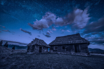 Abandoned wooden houses on a hill under the night starry sky