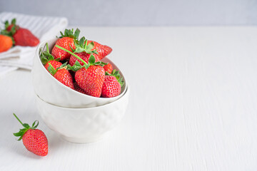 Fresh organic garden strawberries with characteristic aroma, bright red color, juicy texture, and sweetness, source of vitamin C  served in bowls on white wooden table. Image with copy space