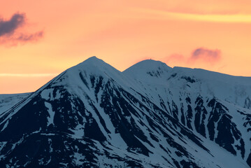 Fototapeta na wymiar Stunning pastel skies in northern Canada with peach sky behind epic snow capped mountains at sunset. Great for wallpaper, office, desktop peaks shot. 