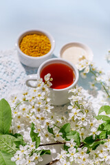 A bowl of pollen, aromatic herbal tea and white honey. Still life in a rustic style with a branch and flowers of a bird cherry and with a white knitted napkin. 