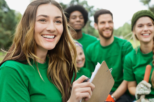 Happy beautiful environmentalist holding clipboard with volunteers in background