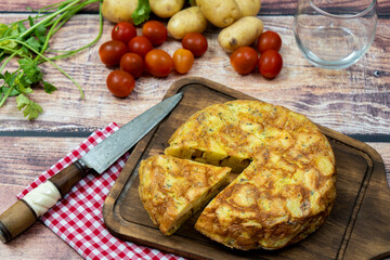 Almost overhead view of a typical Spanish potato omelette with a separate portion with potatoes and cherrie tomatoes in a rustic setting. Traditional Spanish cuisine.