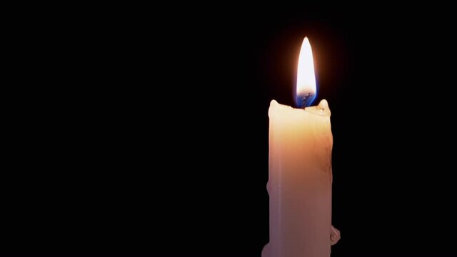 Candle, with Dripping Wax, Burns with a Calm, Yellow Fire on a Black Background. White paraffin candle in dark room. Drips wax. The concept of memory, ritual, celebration. Slow motion.