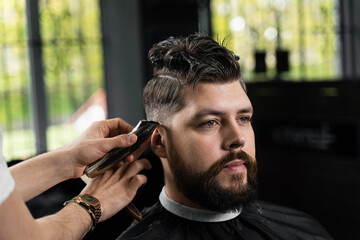 Low fade machine haircut for handsome bearded man in barbershop. Hair cut with a smooth transition.