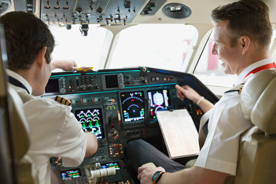 Male pilot and copilot checking instrument panel in airplane cockpit