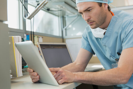 Serious male surgeon using digital tablet at desk in clinic