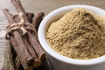 Powder in bowl and dried sticks of liquorice root on table, closeup