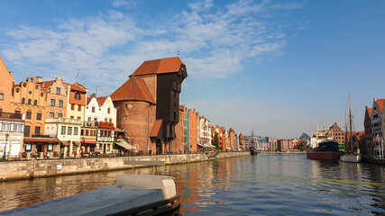 A panoramic view on the shores of Martwa Wisla flowing through Gdansk in Poland, with medieval port crane. New architecture meeting with medieval constructions. Sunny day. Calm water. City tour