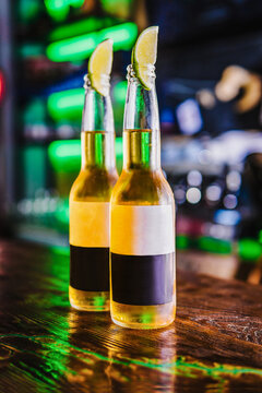 Cold light beer in bottles on the bar. Lime wedges cover the necks of the bottles.