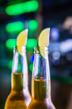 Cold light beer in bottles on the bar. Lime wedges cover the necks of the bottles.