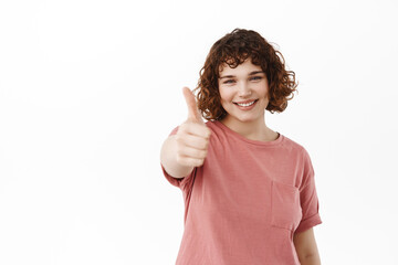 Portrait of smiling young woman extends her hand with thumb up to praise something good, compliment...