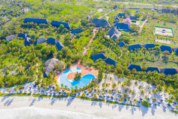 Aerial view of tropical sandy beach with palms and umbrellas at sunny day. Summer holiday on Indian Ocean, Zanzibar, Africa. Landscape with palm trees, hotels, pool, white sand, azure sea. Top view