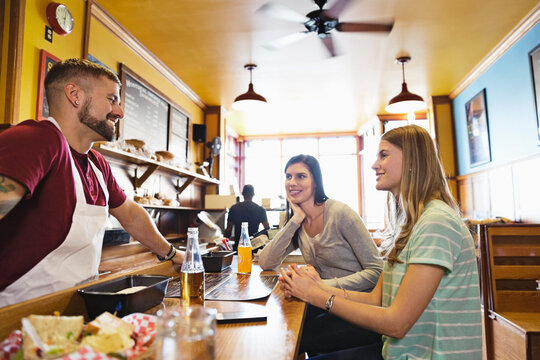 Male Deli Owner Talking To Customers At Deli Counter