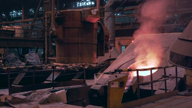 Filled with molten liquid metal ladle container moving on beam crane from blast furnace in foundry metallurgical plant workshop.