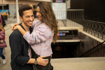 A couple in a romantic moment smiling and looking to each other front of a subway station